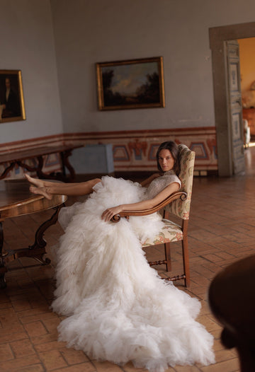 Bride sitting on chair wearing Wona Concept Mars Ivory wedding dress with ruffle layers sold by le reve boutique st albert alberta